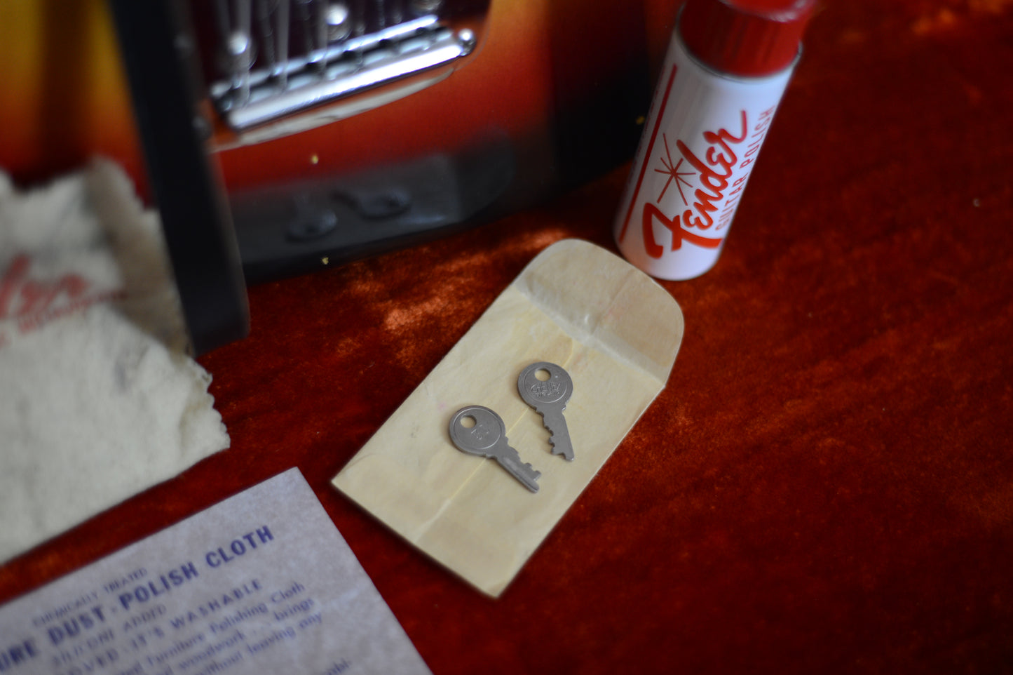 Two keys on a packet with a can of Fender polish and a polishing cloth on a red surface.