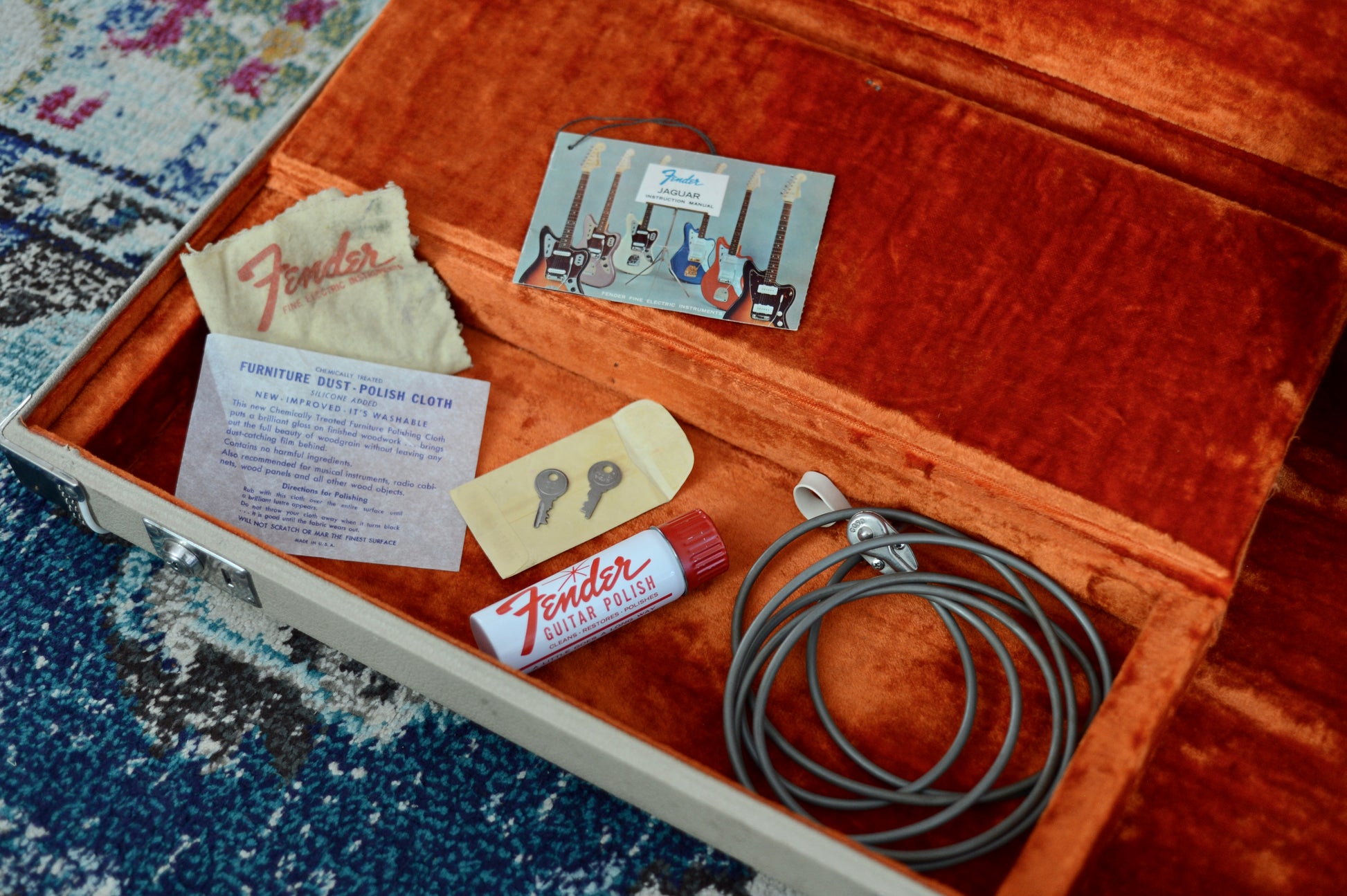 Fender guitar care kit with polish, cloth, and other items in an open wooden box on a textured surface.