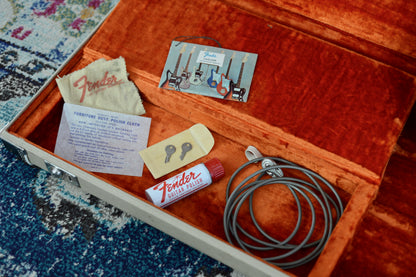Fender guitar care kit with polish, cloth, and other items in an open wooden box on a textured surface.