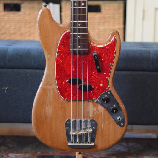 Wooden bass guitar with a red pickguard on a blurred background