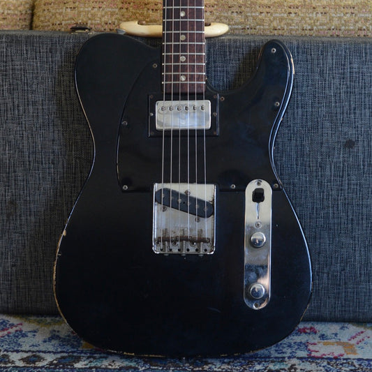 Black electric Fender Custom Telecaster with a worn finish on a textured surface