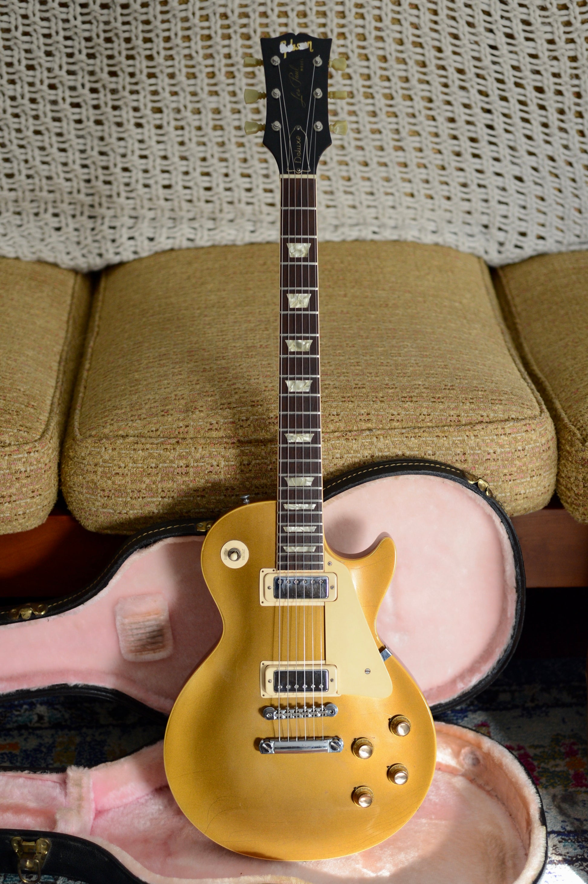 Gold electric Les Paul Deluxe guitar on a pink cushion with a textured wall background